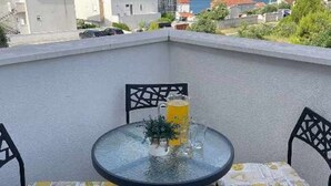 Un pequeño balcón al aire libre con una mesa redonda de vidrio, dos sillas y una planta en maceta.