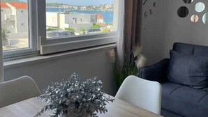 Una habitación con un ventanal grande que ofrece vistas a edificios y una masa de agua. Hay una mesa de comedor con sillas y una planta decorativa en el centro.