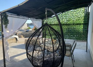 A hanging chair under a covered patio area with a view of a green hedge and a body of water in the background. - Apartments J&M 2 - One Bedroom Apartment with Terrace (Rogoznica)