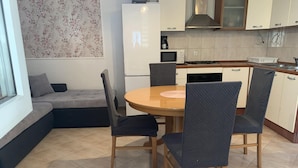 A modern kitchen with a dining area, featuring a round wooden table, dark chairs, and a built-in oven. - Apartments J&M 2 - One Bedroom Apartment with Terrace (Rogoznica)