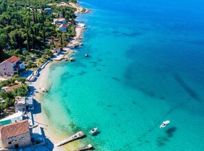 An aerial view of a coastal area with clear turquoise waters, a sandy beach, and several buildings along the shore. - Apartment Gabrijela - One Bedroom Apartment with Sea View (Slano)