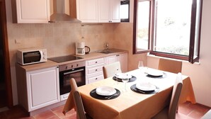 Una cocina compacta con armarios blancos, un microondas, una cafetera y una mesa de comedor para dos.