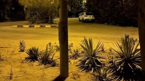 A nighttime view of a parking lot with a white car parked in the distance, surrounded by desert vegetation and a building with illuminated windows. - 819 · 2BR Townhouse | Garden | Sleeps 5 (Sheikh Zayed City)