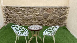 A small outdoor seating area with two white chairs and a round table, set against a stone wall and green artificial turf. - 819 · 2BR Townhouse | Garden | Sleeps 5 (Sheikh Zayed City)
