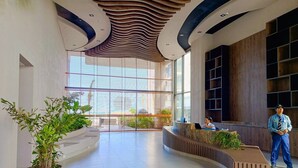 Um lobby moderno com balcão de recepção curvo, grandes janelas e plantas internas.