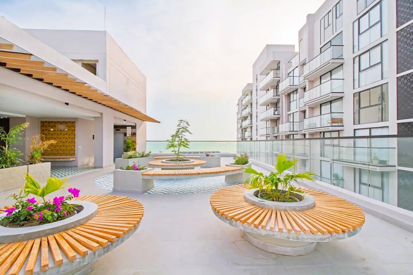 A rooftop terrace with circular wooden seating areas, potted plants, and a view of the sea.