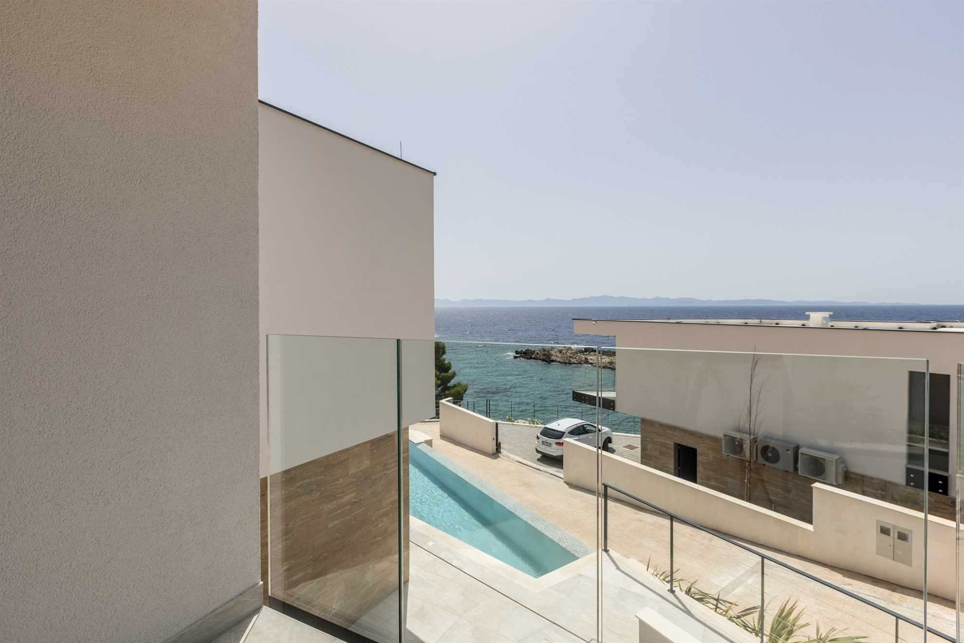 Eine moderne Wohnung mit einem Glasbalkon mit Blick auf einen Swimmingpool und das Meer.