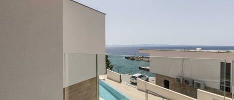 Eine moderne Wohnung mit einem Glasbalkon mit Blick auf einen Swimmingpool und das Meer.