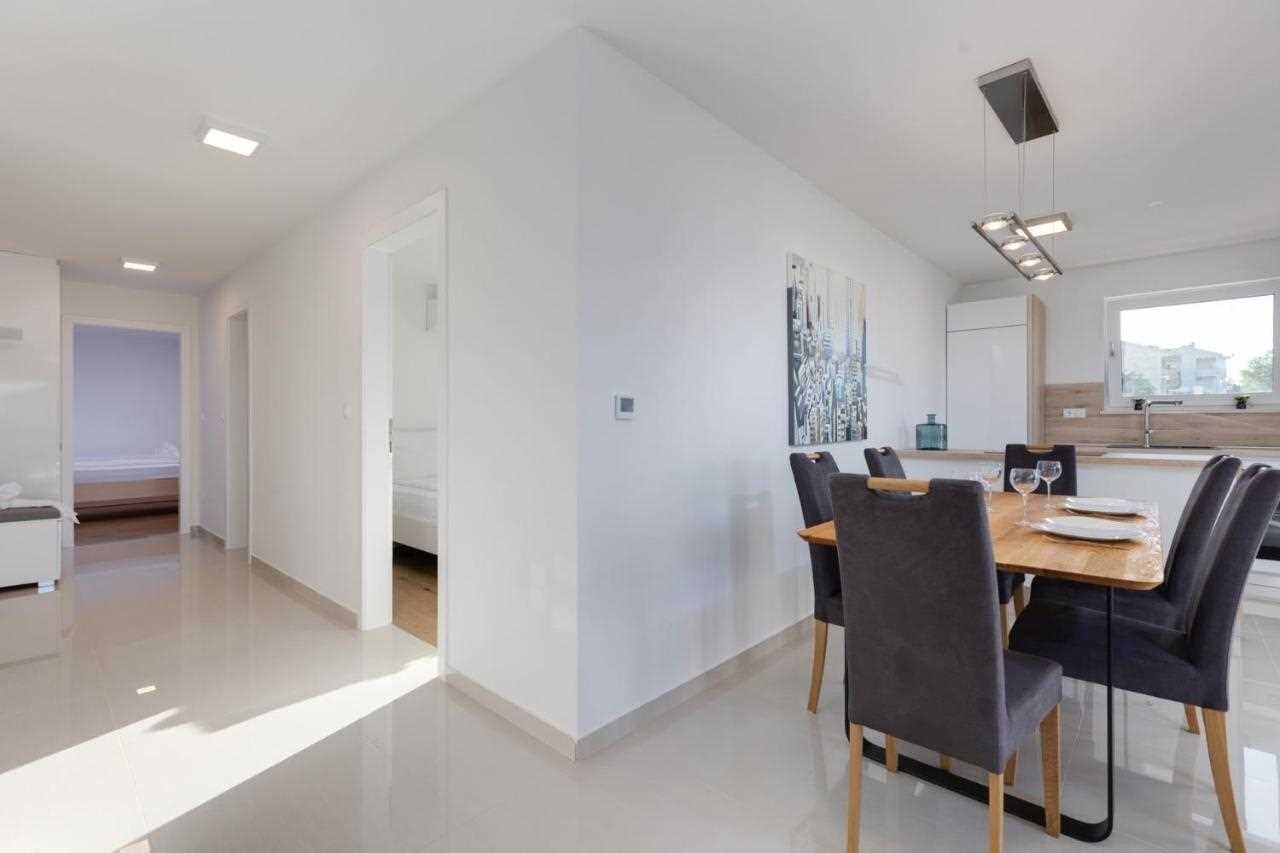 Uma zona de refeições moderna com mesa e cadeiras de madeira, cozinha ao fundo e ambiente claro e bem iluminado.