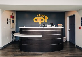 Un mostrador de recepción con acabado en madera oscura, un letrero que dice "stay apt SUITES" y un teléfono.