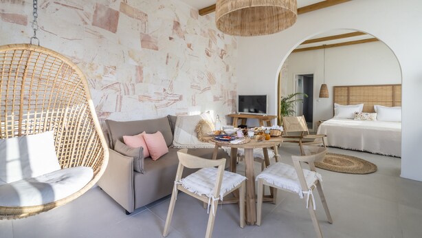 A modern room with a hanging chair, a sofa, a dining table with chairs, and a bed with a wooden headboard. - Sirma Beach House (Kimolos)