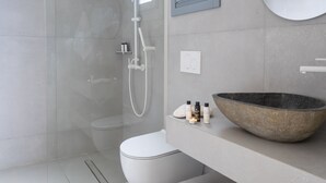 Un baño moderno con ducha de vidrio, inodoro blanco, lavamanos redondo grande y un espejo en la pared.