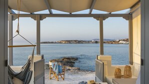 A covered outdoor seating area with a view of the sea, a hammock, and a table with a hat and a stone. - Sirma Beach House (Kimolos)