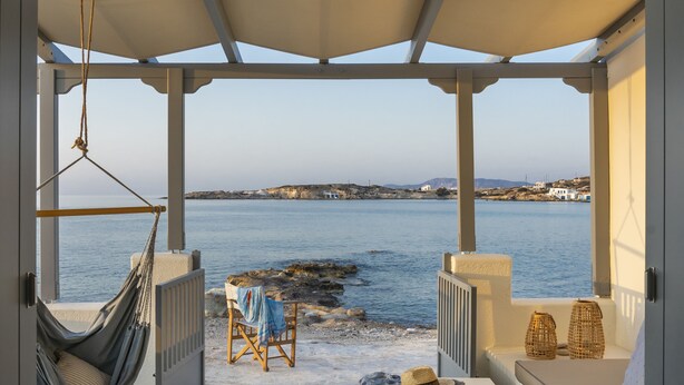 Un área de estar techada al aire libre con vista al mar, una hamaca y una mesa con un sombrero y una piedra.