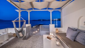 Una terraza con vista al mar, muebles blancos y una silla colgante.