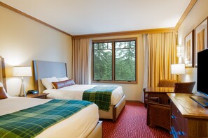 Quarto de hotel com duas camas, uma escrivaninha, uma cadeira, televisão e janela com cortinas.