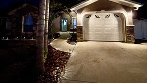 Eine Garage mit weißer Tür, einer Auffahrt und einem gut beleuchteten Eingang.