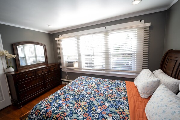A bedroom with a large bed, a dresser, and a window with blinds.