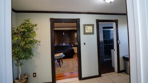 A hallway with a plant, a dining area with a table and chairs, and a room with a bed and a window.