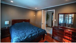 A bedroom with a bed, dresser, lamp, and a door leading to another room.