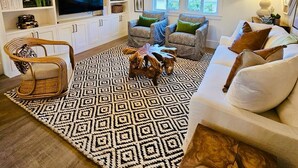 A living room with a patterned rug, white sofas, a TV, and a bookshelf. - Newly Renovated, Little Palm Cottage with dock slip, Elbow Cay  (Elbow Cay)