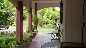 A covered outdoor area with a concrete floor, potted plants, and a white chair.