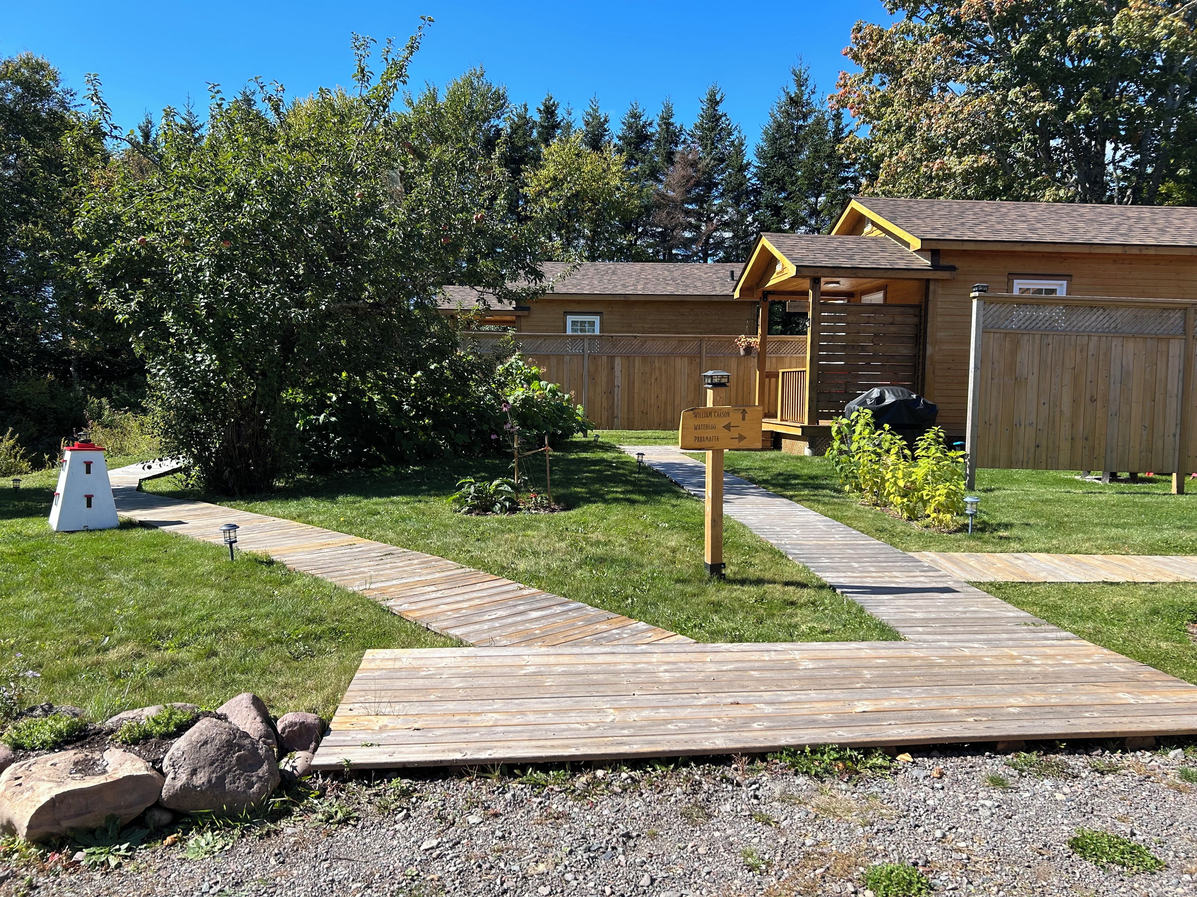 A wooden cabin with a deck, surrounded by a grassy yard and trees.