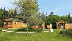 Una hilera de cabañas de madera con un patio cubierto de césped y un árbol en el centro.