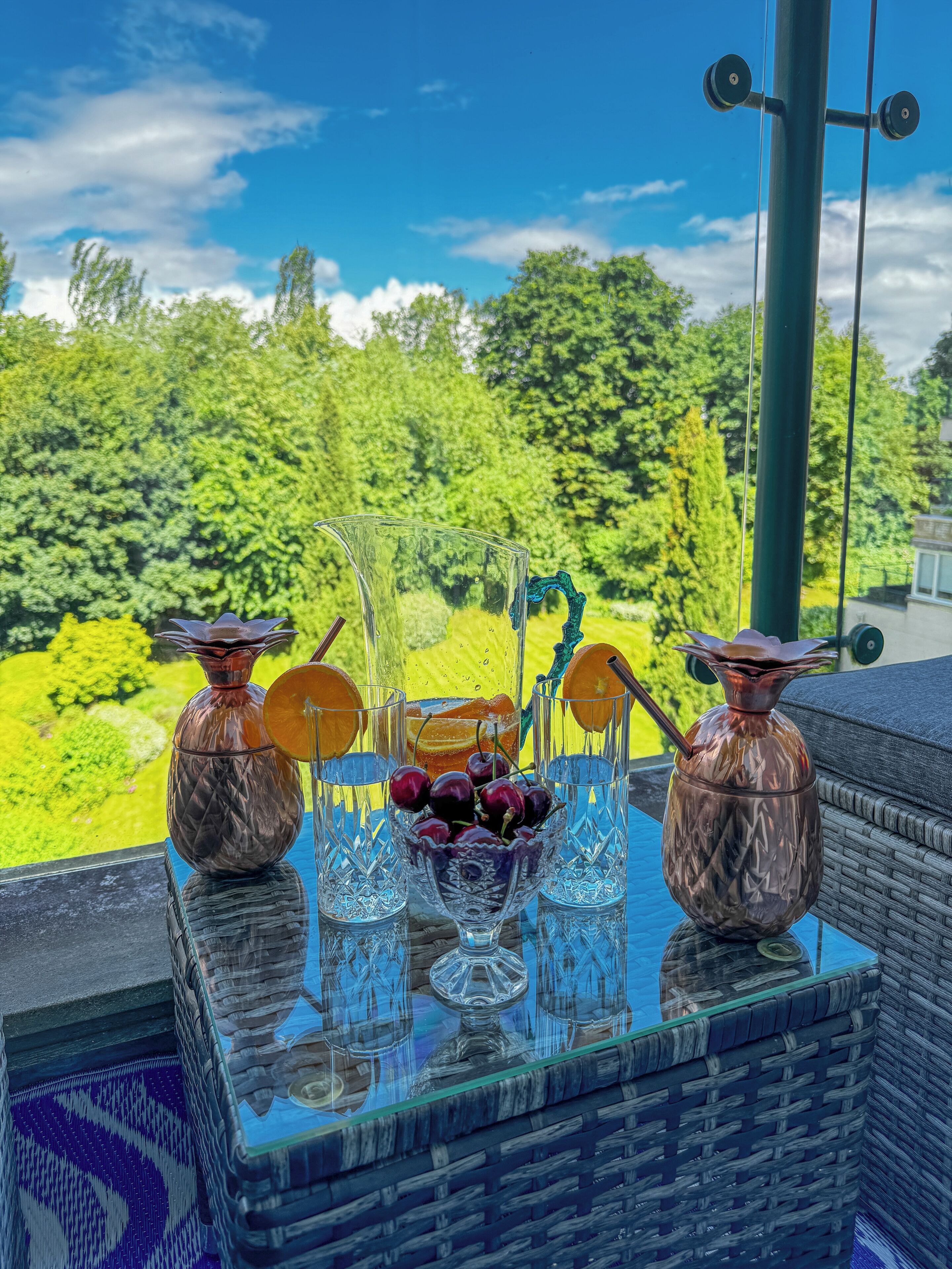 Un tavolo in vetro con vista su un giardino rigoglioso e un cielo azzurro.