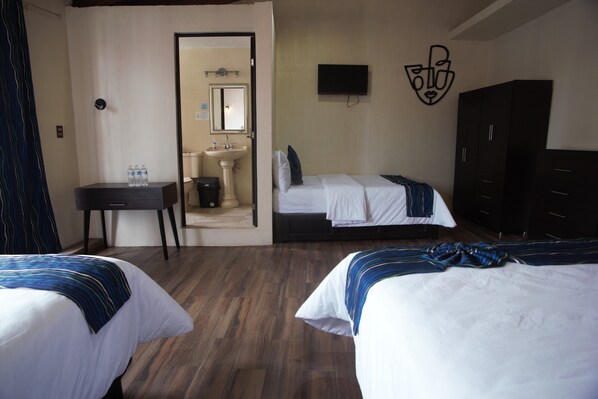 A hotel room with two beds, a desk, a bathroom visible through an open door, and a TV mounted on the wall. - Capital O Casa Rotter (San Cristóbal de las Casas)
