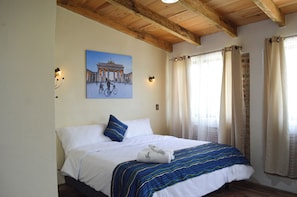 A hotel room with a bed, a painting of a building, and a window with curtains. - Capital O Casa Rotter (San Cristóbal de las Casas)