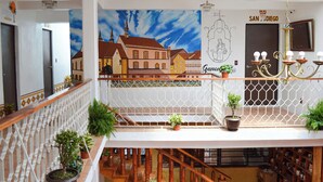 Interior con varios niveles, un mural de un pueblo, una araña y plantas en macetas.