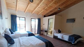Habitación de hotel con dos camas, un escritorio, un televisor y un balcón con cortinas.