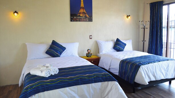 Habitación de hotel con dos camas, ropa de cama a rayas, una mesita de noche con una figurita y un cuadro de la Torre Eiffel.