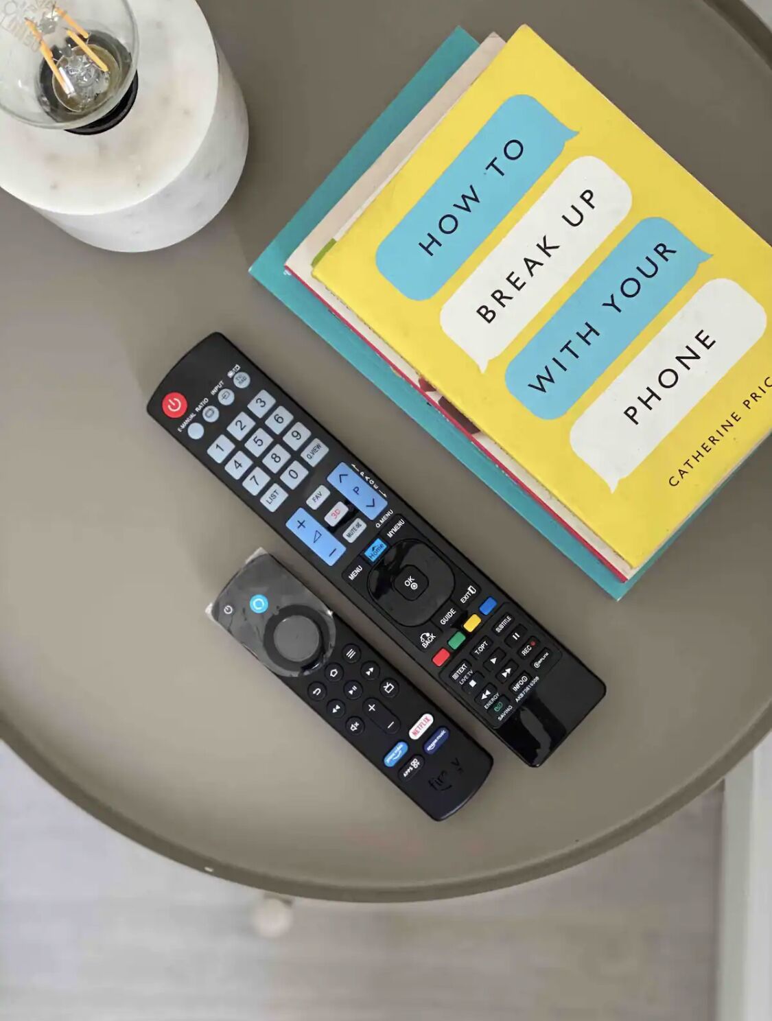 Une table avec deux télécommandes et un livre intitulé « Comment se déconnecter de son téléphone », de Catherine Price.