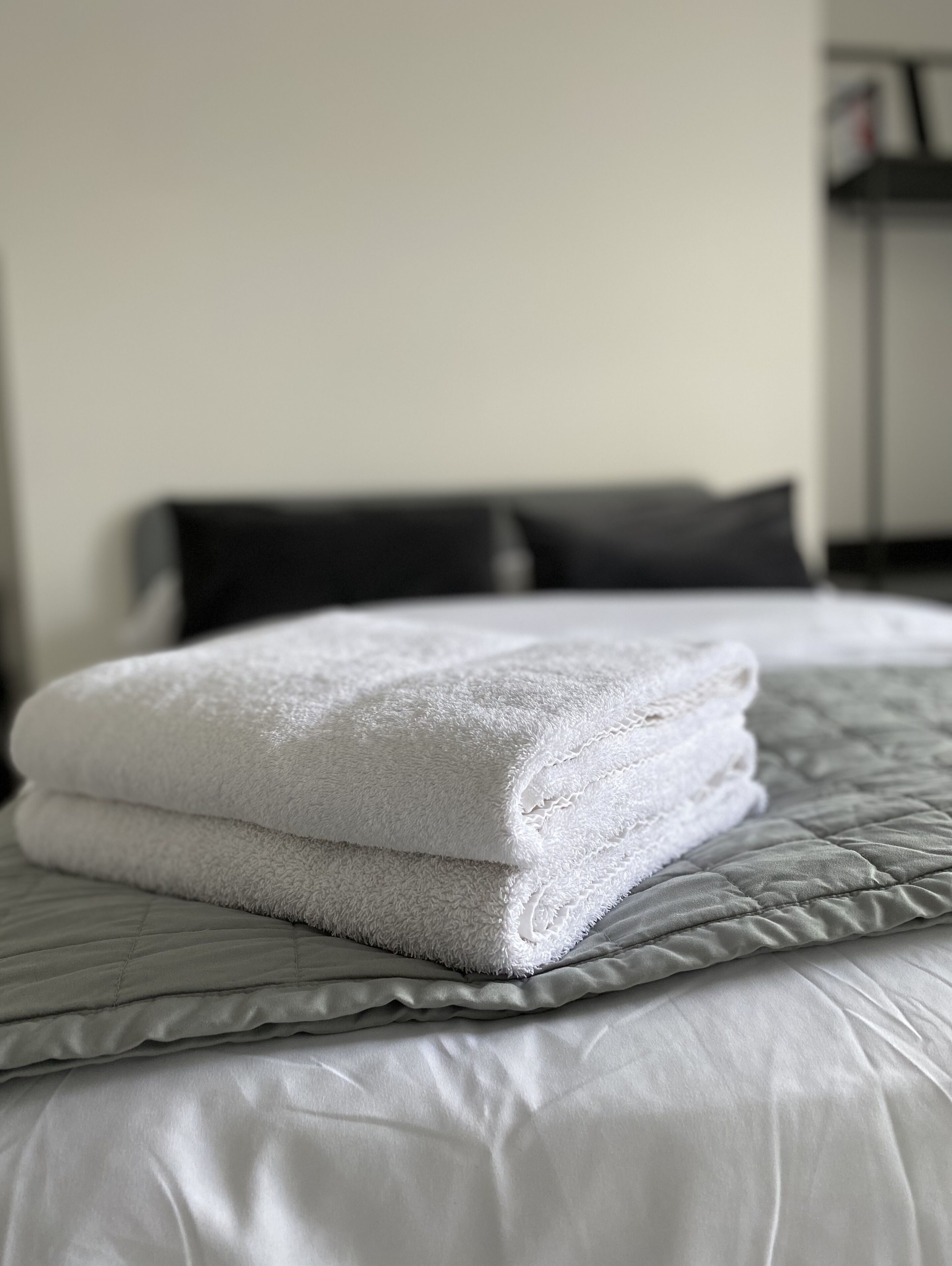 A neatly made bed with a folded white towel and a grey quilted blanket.