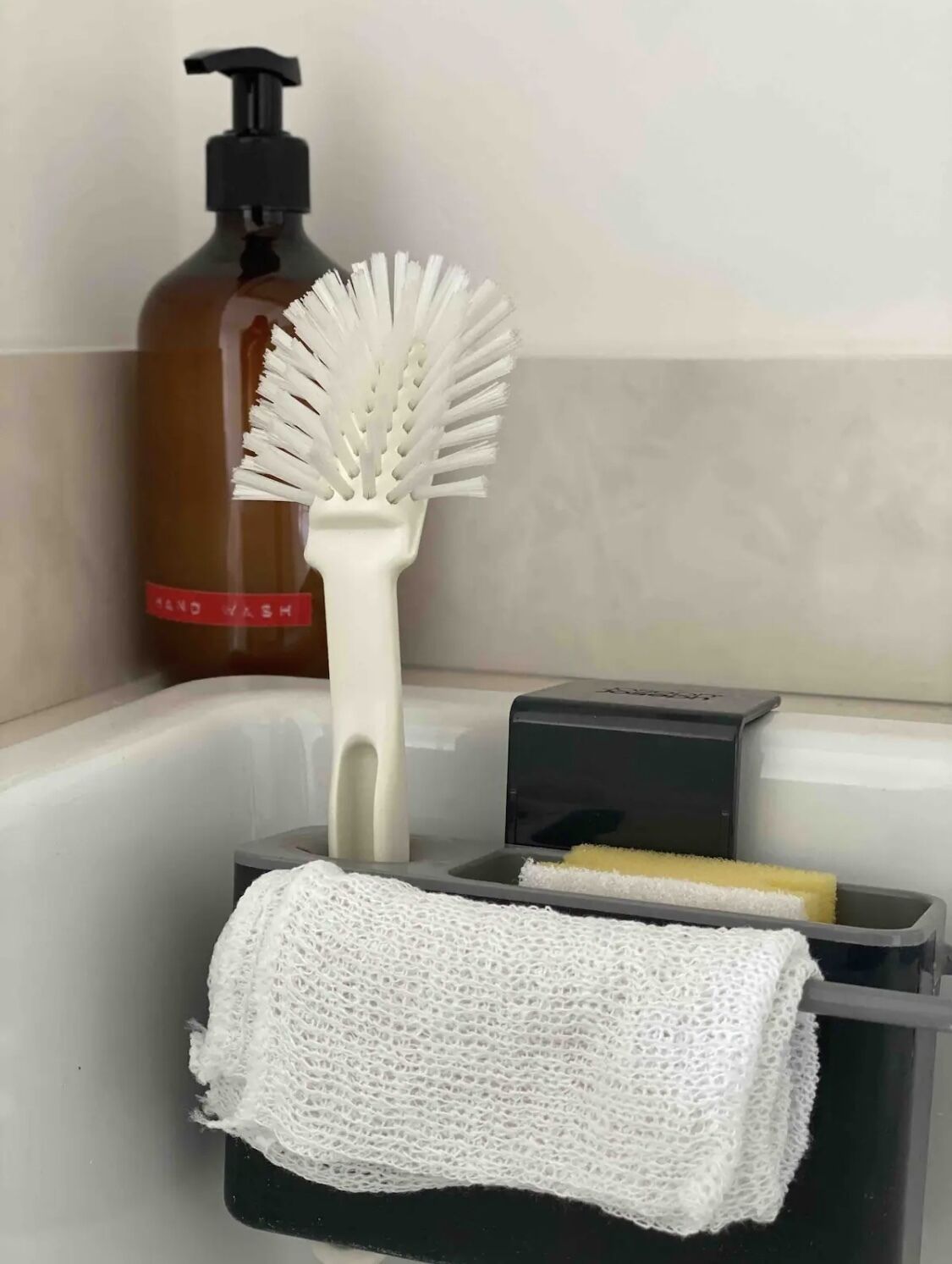 Um banheiro com toalha branca, escova branca, dispensador de sabonete e esponja em um recipiente preto.