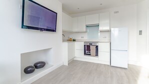 Una cuina moderna amb els armaris blancs, forn integrat i un gran televisor de pantalla plana penjat a la paret.