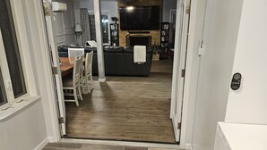 Un interior moderno con piso de madera, un comedor con mesa y sillas, una sala de estar con sofá y televisor, y una cocina con refrigerador y microondas.