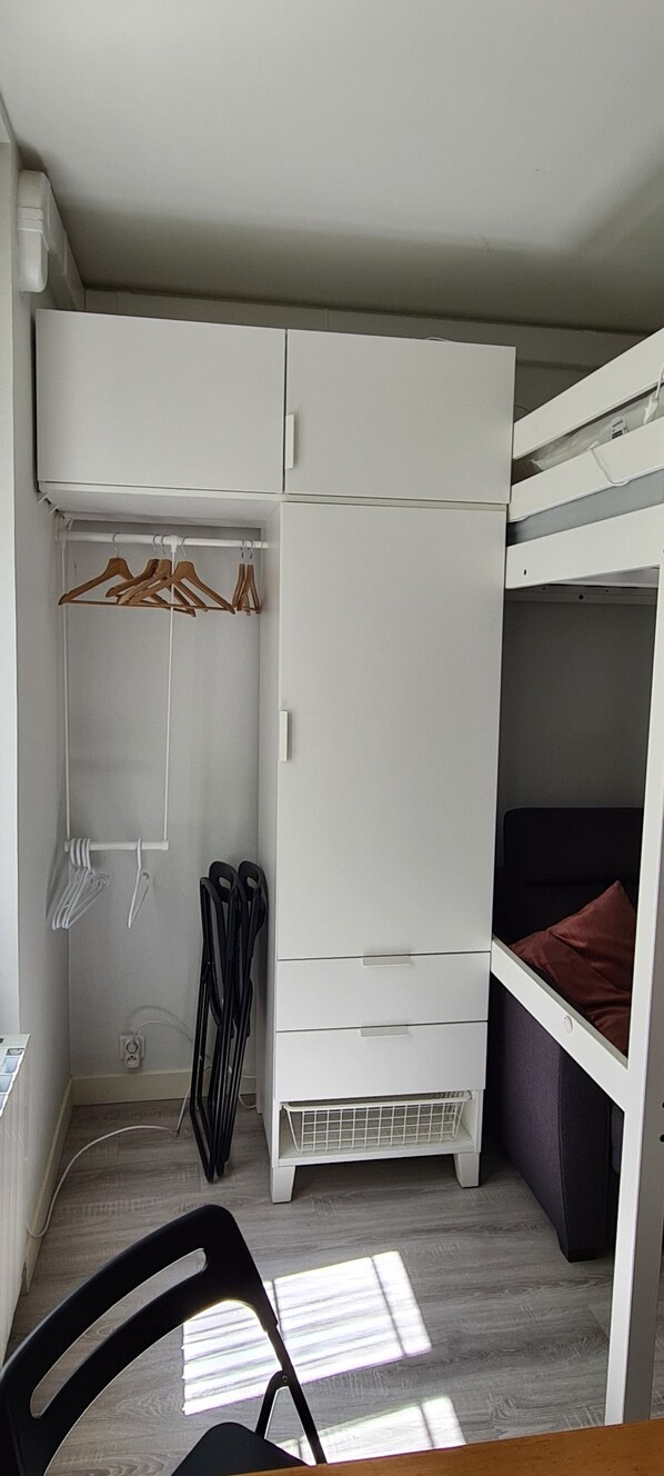 Une petite pièce comprenant un lit superposé, une armoire blanche et une chaise.