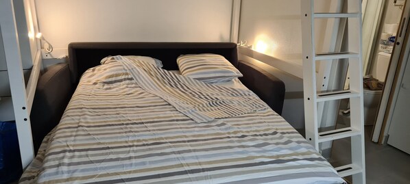 A single bed with a striped bedspread and pillows, a bedside table with a lamp, and a white ladder against the wall. - Studio 2 à 4 Personnes, Paris 7e (Paris)