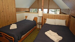 Quarto com duas camas, paredes de madeira, uma janela e um abajur.