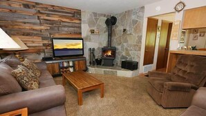 Un salon chaleureux avec un mur en pierre, une cheminée, un canapé, un fauteuil inclinable et un téléviseur.