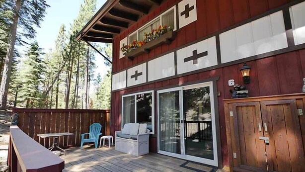 Une terrasse en bois dotée d’un espace salon couvert, d’une porte-fenêtre coulissante et d’une petite table et d’une chaise d’extérieur.