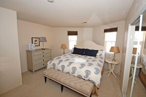 Un dormitorio con cama, un banco, cómoda, dos lámparas y un espejo.