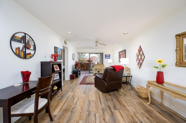 A spacious living room with a wooden floor, a brown leather sofa, a dining table with chairs, and a TV.
