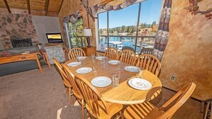 A dining area with a large wooden table set for six, surrounded by wooden chairs, with a stone wall and a fireplace in the background. - Waterfront Home with Mountain Inspired Decor, Private Hot Tub and Boat Dock 2085S~ (South Lake Tahoe)