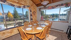 A dining area with a wooden table and chairs, large windows with a view of mountains and trees, and a sign for rentals. - Waterfront Home with Mountain Inspired Decor, Private Hot Tub and Boat Dock 2085S~ (South Lake Tahoe)