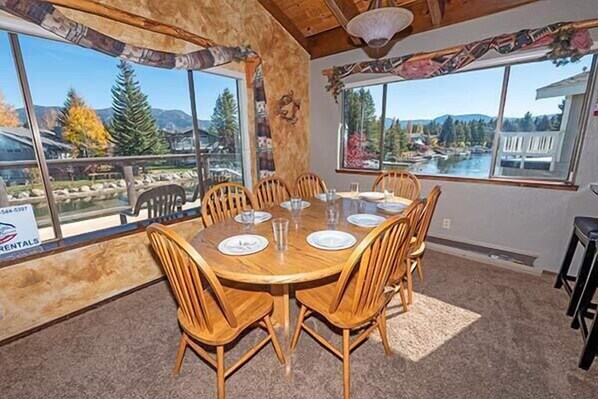 A dining area with a wooden table and chairs, large windows with a view of mountains and trees, and a sign for rentals.