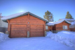 Eine Holzhütte mit schneebedecktem Dach, einer Garage und einer kleinen Veranda.